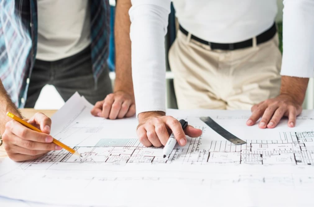 Two people discuss over architectural plans on a desk