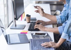 People work at computers, a man's hand rests on papers