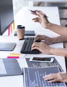 People work at computers, a man's hand rests on papers