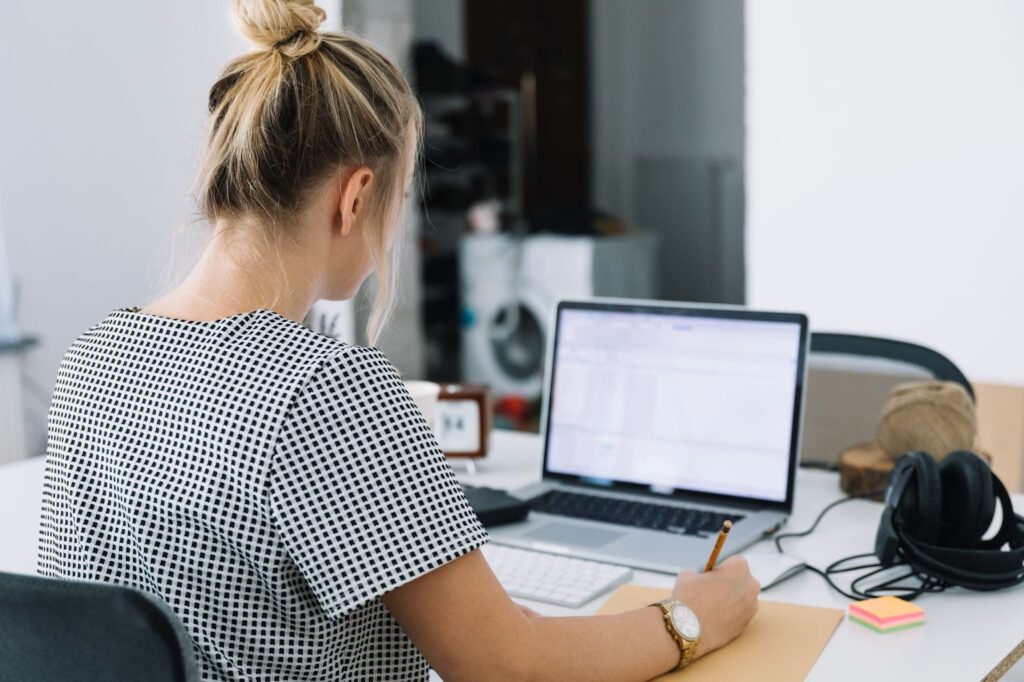 Businesswoman writing notes over brown paper with laptop on desk