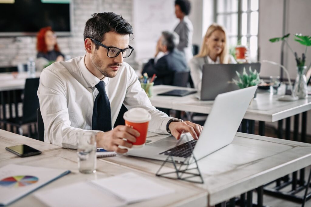 Man sitting in the office and working on laptop while drinking coffee